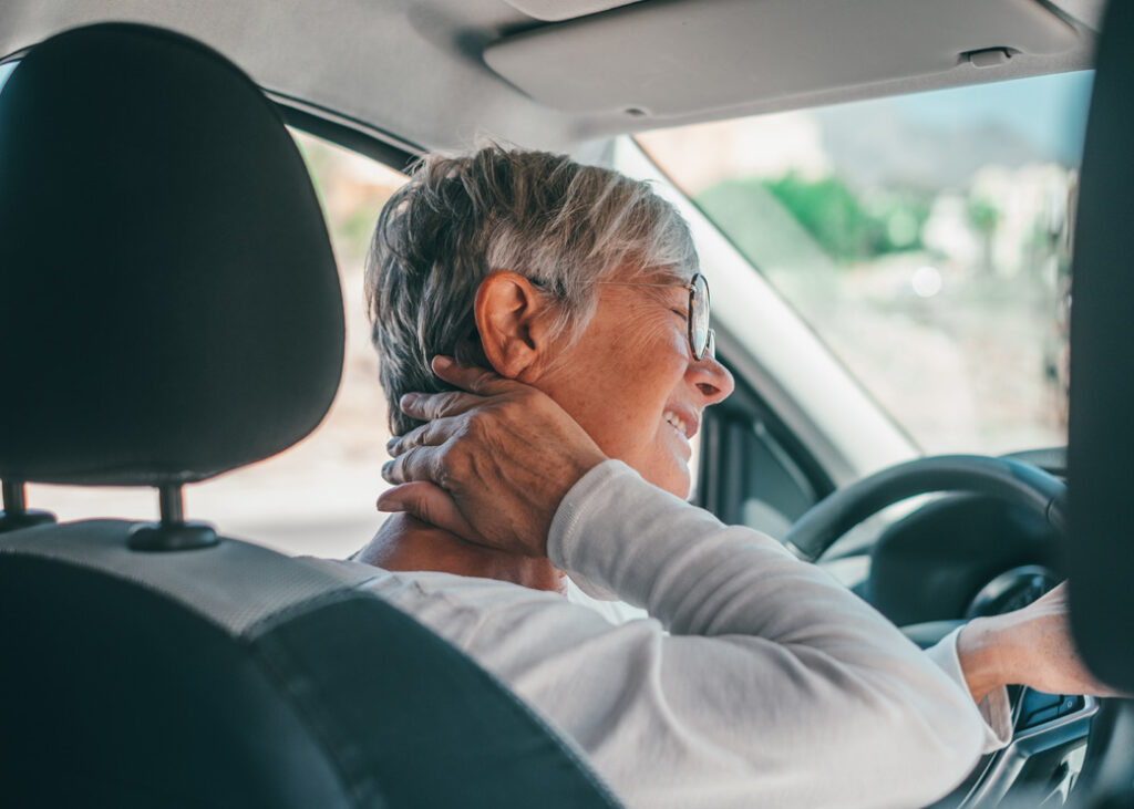 old woman having neck pain while driving a car