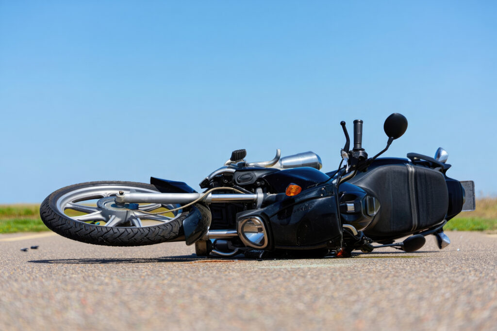 Black motorcycle accident on road surface under clear blue sky.
