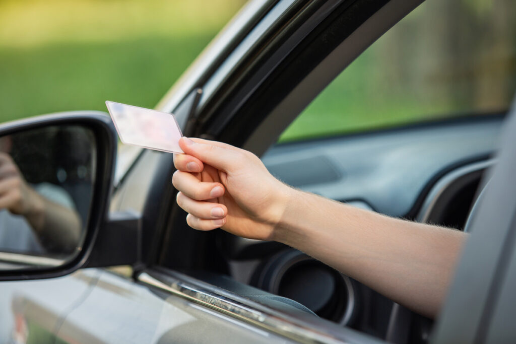 Close up person hand out of the car window holding the driver license as shows it to the police officer for control