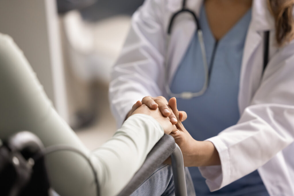 Sympathetic doctor giving comfort, psychological help to woman with disability, touching hand of patient sitting in wheelchair, expressing support, motivating for recovery. Cropped close up shot