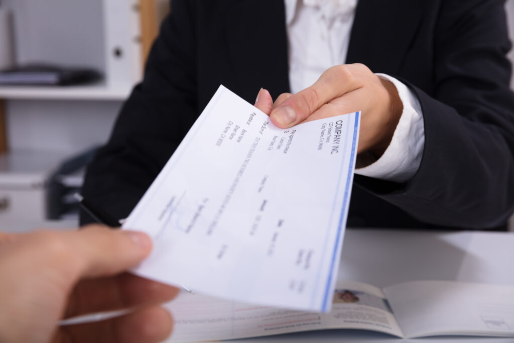 Close-up Of A Business Woman Handing Over Cheque To Her Colleague At Workplace
