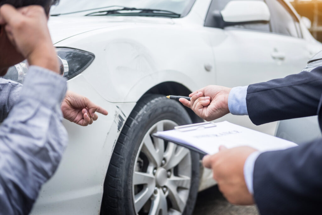 Insurance agent writing on clipboard while examining car after a