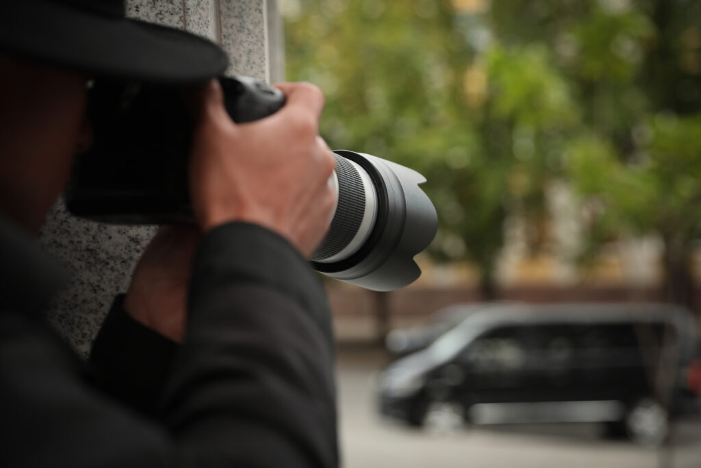 Private detective with modern camera spying on city street, closeup