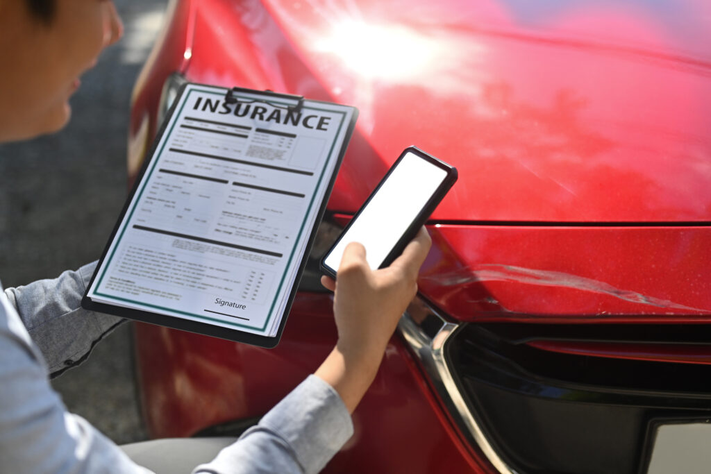 Insurance adjuster reviewing a claim form and using a smartphone after inspecting a damaged car