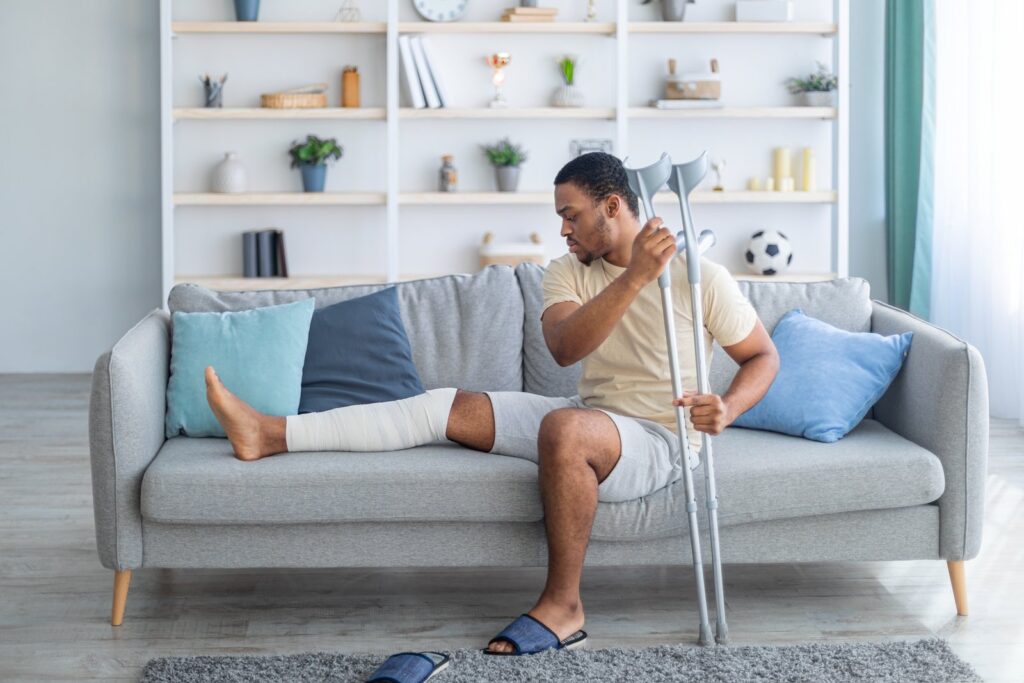 Man with a leg injury sitting on a sofa at home, unable to perform normal household tasks